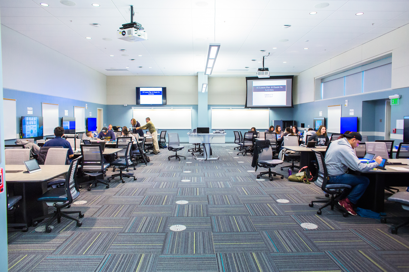 Students working in a TEAL room with eight tables, a projector, and nine monitors
