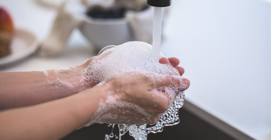 Picture of an adult waking their hands under a sink with lots of foamy bubbles
